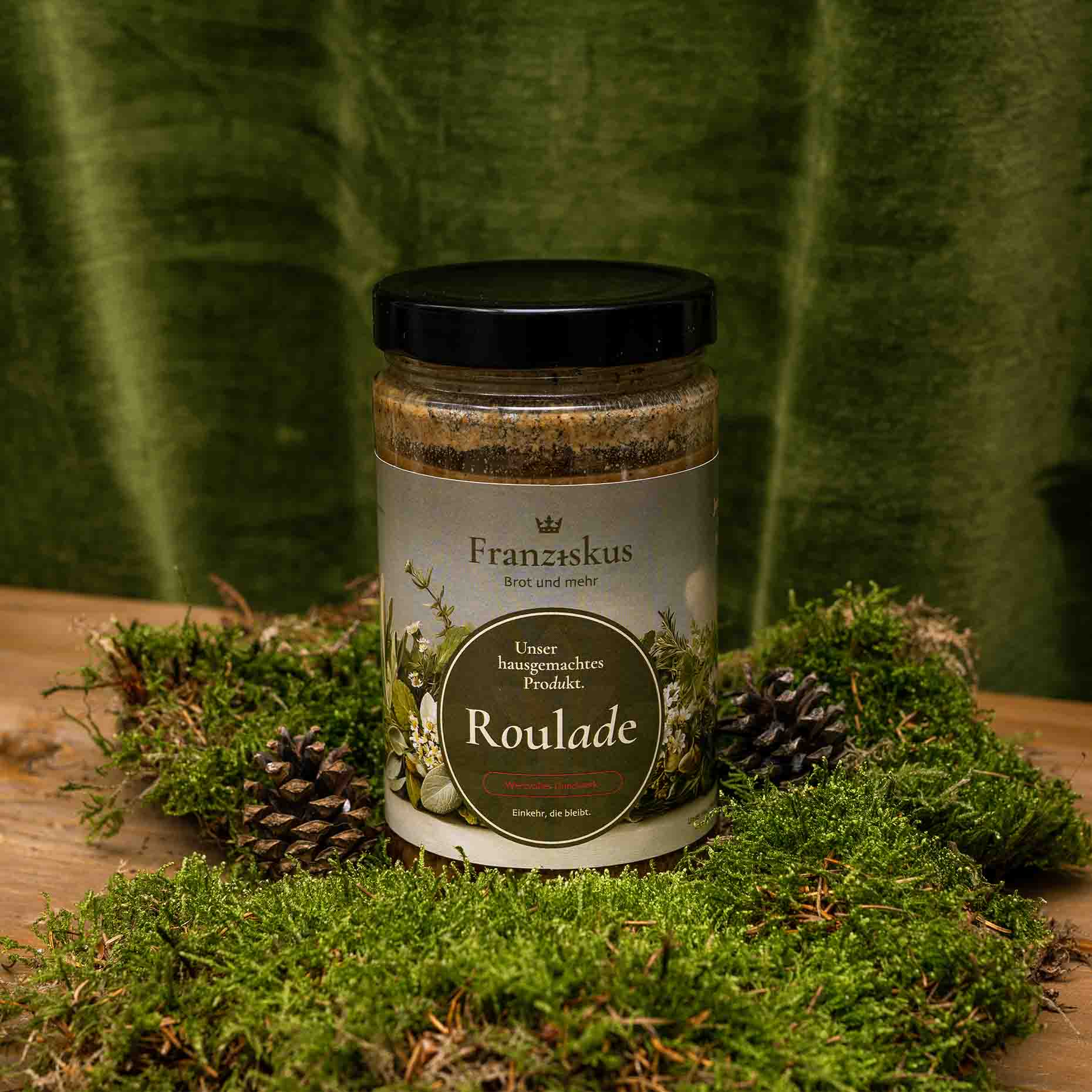Ein Bild des hauseigenen Produkts: Roulade. Dekoriert auf Moos mit Kiefernzapfen und olivfarbenem Hintergrund.