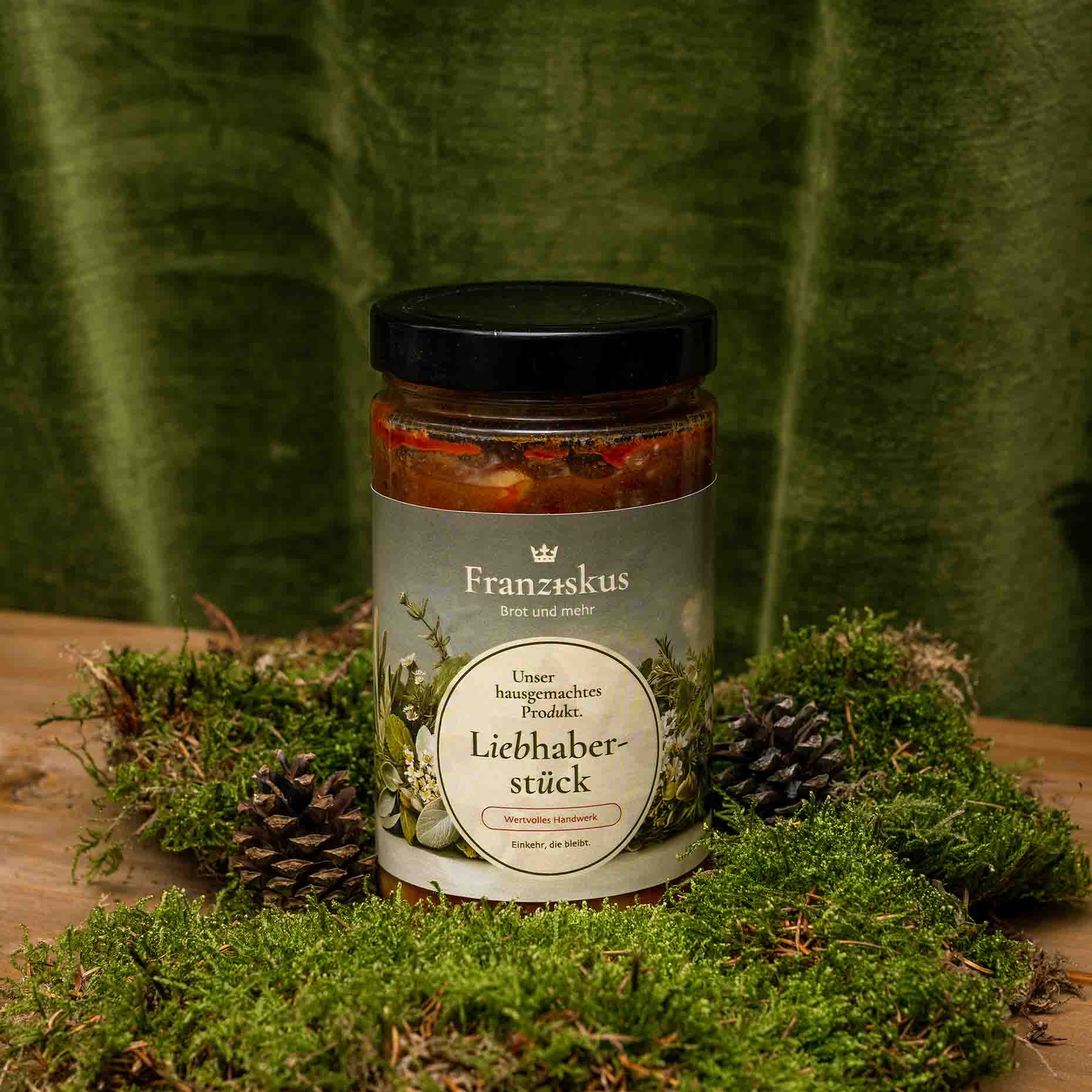 Ein Bild des hauseigenen Produkts: Gulaschsuppe – Liebhaberstück. Dekoriert auf Moos mit Kiefernzapfen und olivfarbenem Hintergrund.